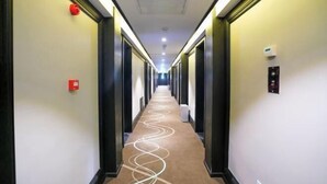 Un couloir d’hôtel avec un sol recouvert de moquette et des portes de chaque côté.