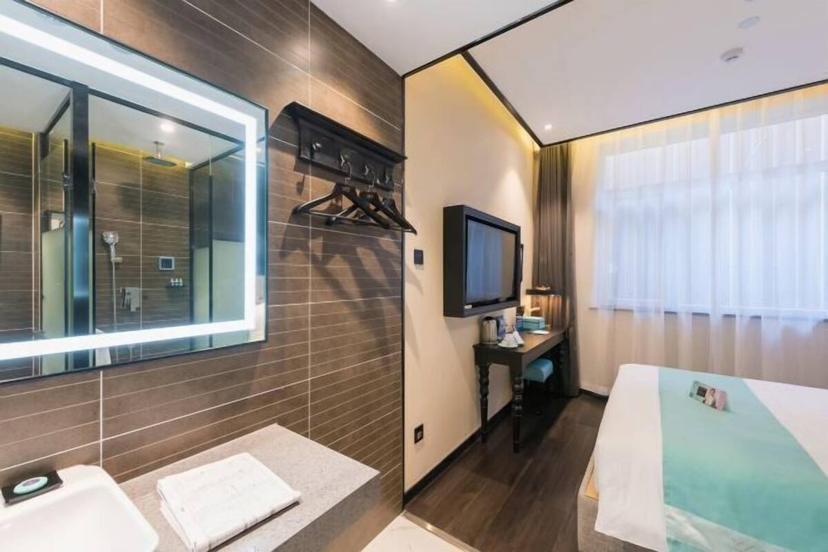 Moderni hotellihuone, jossa on suuri peili, televisio, työpöytä ja sänky.