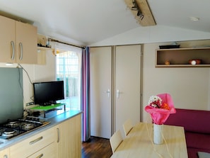 A compact kitchen with a stove, a television on a stand, a dining table with chairs, and a sofa.