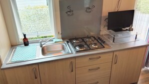 A kitchen with a gas stove, a sink, and wooden cabinets. - Seasonal Mobile Home (Les Arcs)