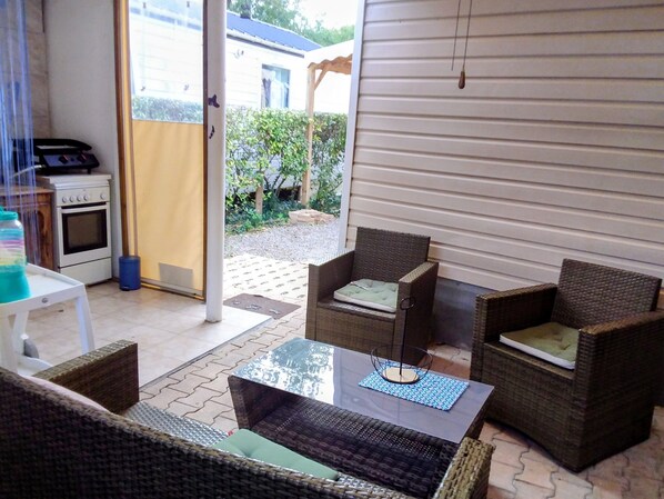 A patio with wicker furniture, a glass table, and a view of a house through a sliding door.