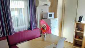 A room with a wooden table, two white chairs, a pink sofa, a microwave, and a small cabinet. - Seasonal Mobile Home (Les Arcs)