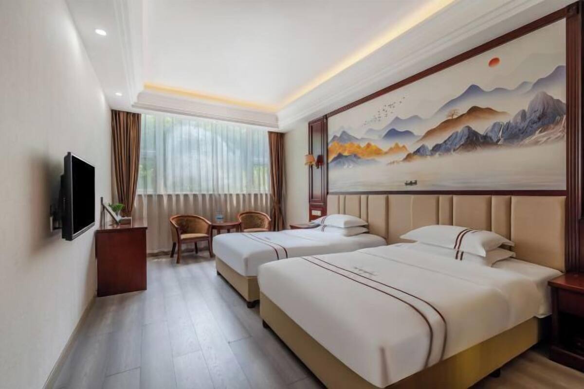 Quarto de hotel com duas camas, televisão, escrivaninha e um quadro grande na parede.