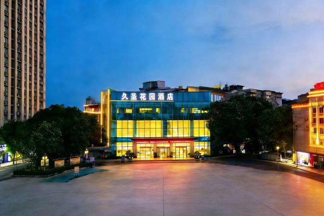 A modern building with a large glass facade, likely a hotel or commercial property, with a spacious outdoor area in front.