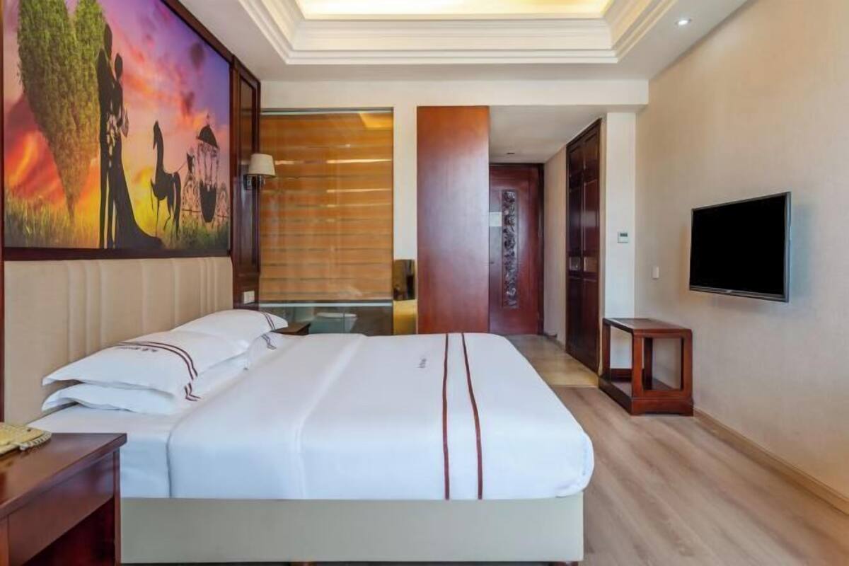 Quarto de hotel com cama, televisão, quadro e piso de madeira.