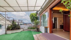 Un patio couvert avec une pelouse artificielle, un banc en bois et une vue sur un immeuble résidentiel.
