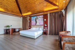Een hotelkamer met een groot bed, houten plafond, een bureau met stoel, een televisiescherm en een gordijn.