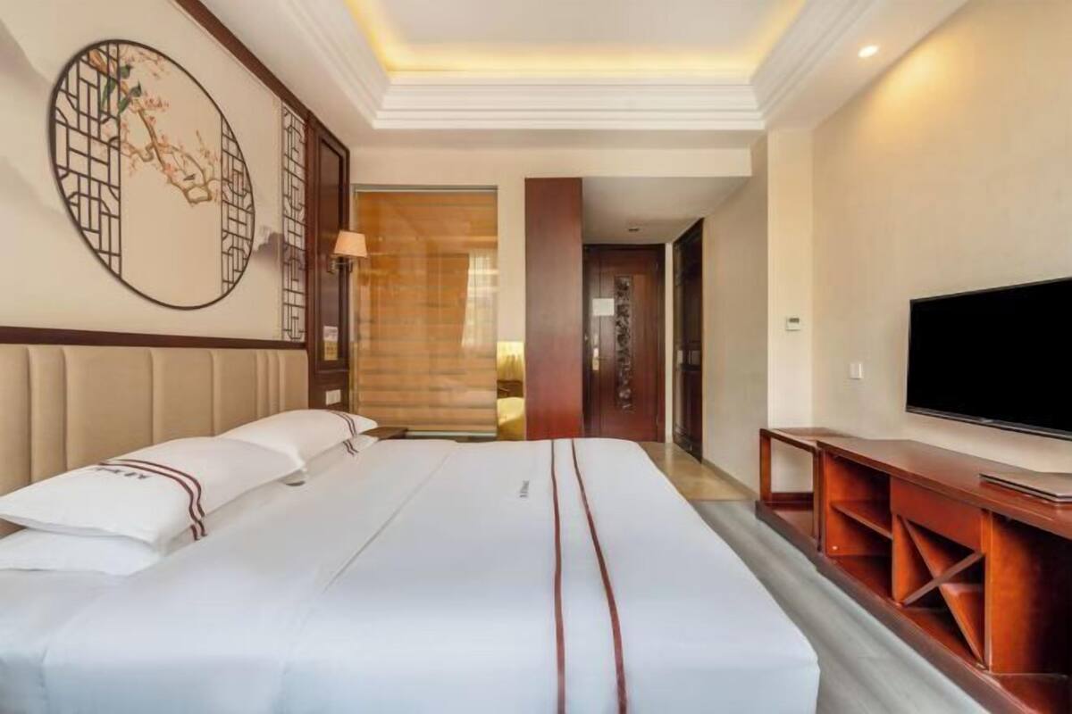 Quarto de hotel com uma cama grande, televisão e um elemento decorativo na parede.