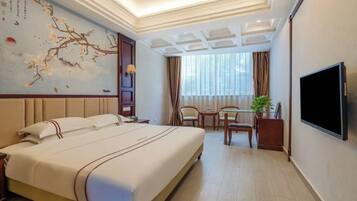 A hotel room with a large bed, a desk with two chairs, a TV, and a decorative wall with a painting.