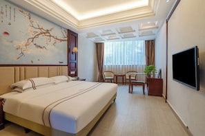 Hotelkamer met een groot bed, een bureau met twee stoelen, een televisie en een decoratieve muur met een schilderij.