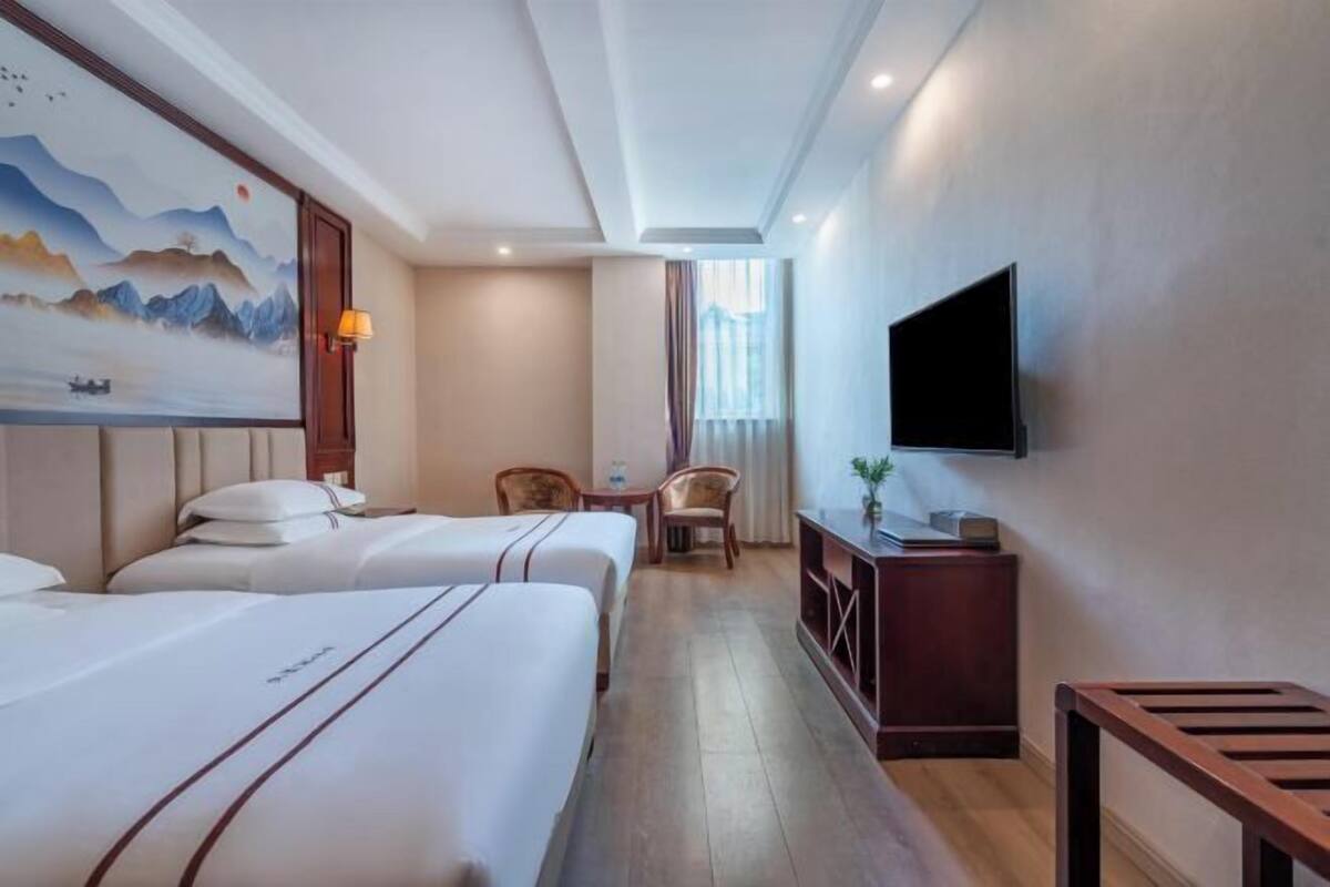 Quarto de hotel com duas camas, televisão, escrivaninha e um quadro na parede.