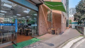 A commercial space with a glass storefront, outdoor seating, and a brick wall.