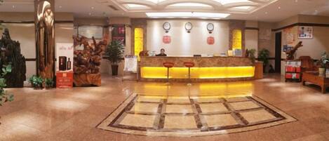 A hotel reception area with a central desk, a large decorative sculpture, and a patterned floor.