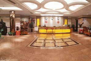 Een hotel receptie met een centraal gelegen balie, een groot decoratief kunstwerk en een vloer met een patroon.