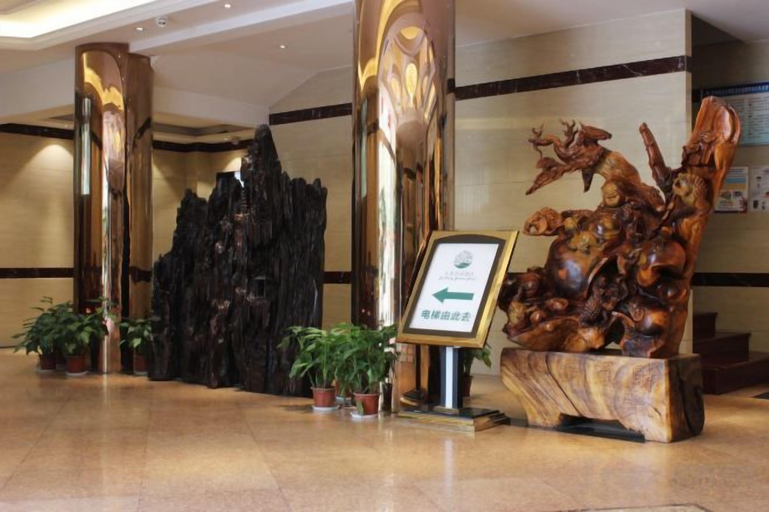 Un hall d’entrée avec un comptoir de réception, une grande sculpture en bois et des plantes en pot.