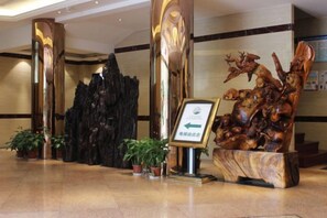Un hall d’entrée avec un comptoir de réception, une grande sculpture en bois et des plantes en pot.