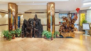 Un hall d’entrée agrémenté d’une sculpture en bois au centre, de plantes en pot et d’un comptoir de réception avec une enseigne.