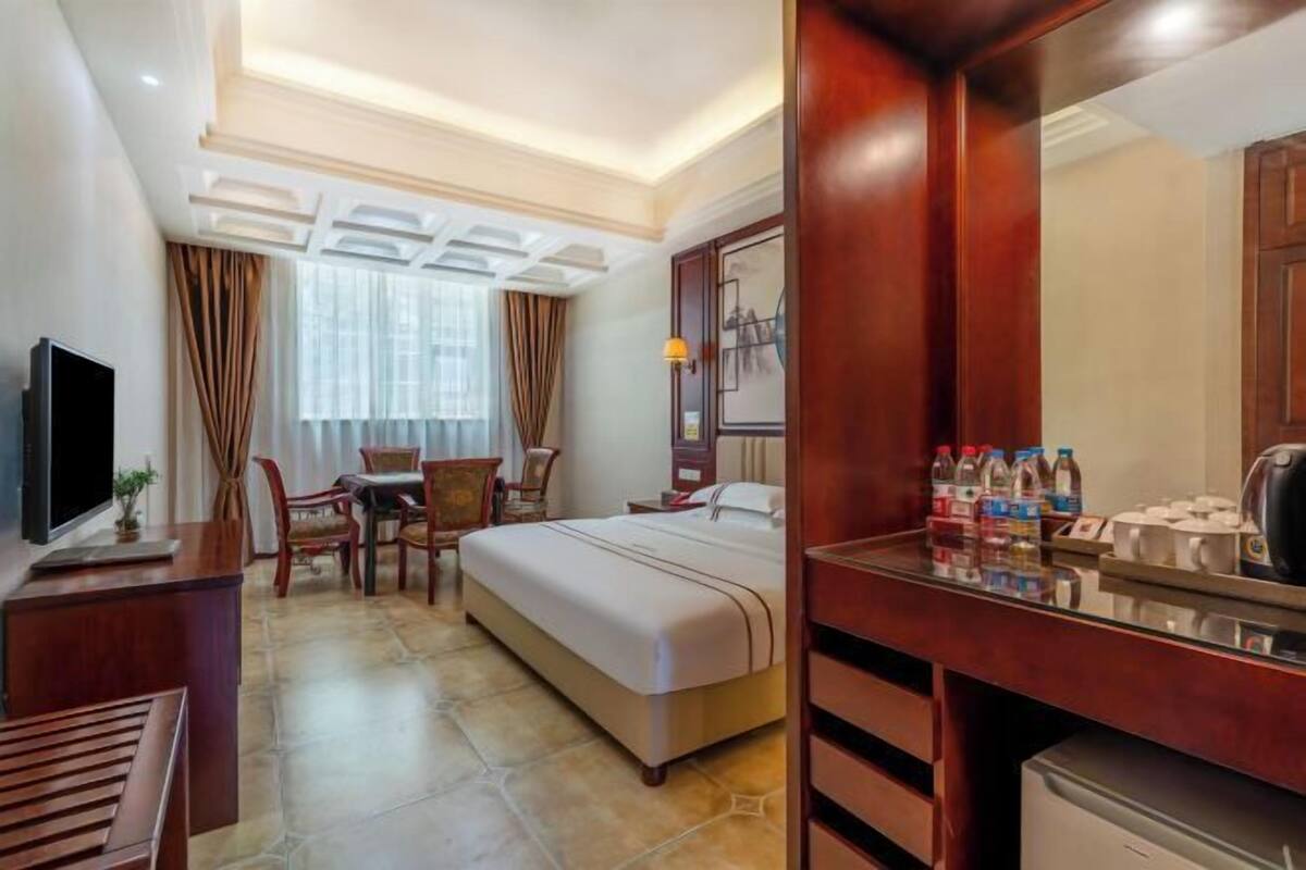 Quarto de hotel com cama, escrivaninha, televisão, área de refeições e banheiro.