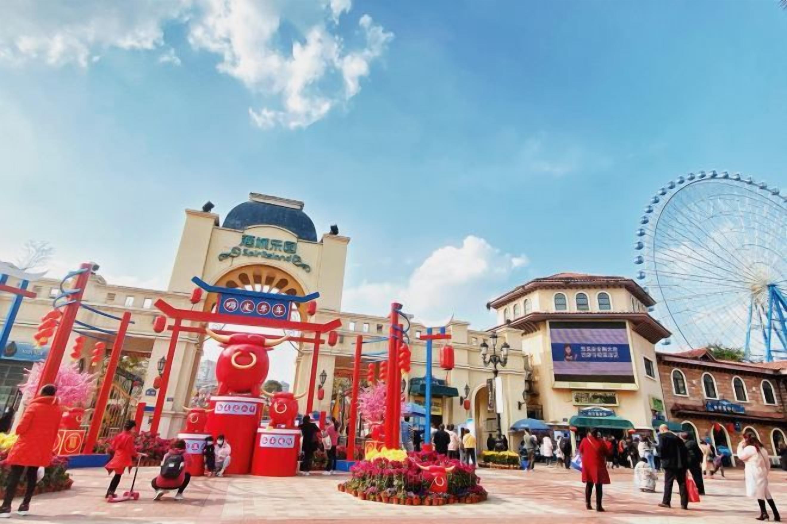 A large building with a prominent entrance, a Ferris wheel in the background, and a clear sky.