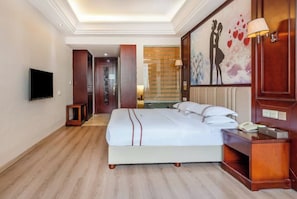 Een hotelkamer met een groot bed, een flatscreen televisie, een nachtkastje en een schilderij aan de muur.