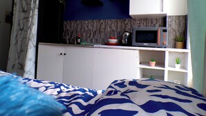 A bedroom with a bed, a kitchenette with a microwave, a kettle, and a shelf with plants. - Santoriniapartmentwestkensingtonsleeps3-ensuite-ac (London)