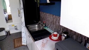 A compact kitchen with a sink, stove, and a small countertop. There is a potted plant on a shelf and a red and white cup on the counter. - Santoriniapartmentwestkensingtonsleeps3-ensuite-ac (London)