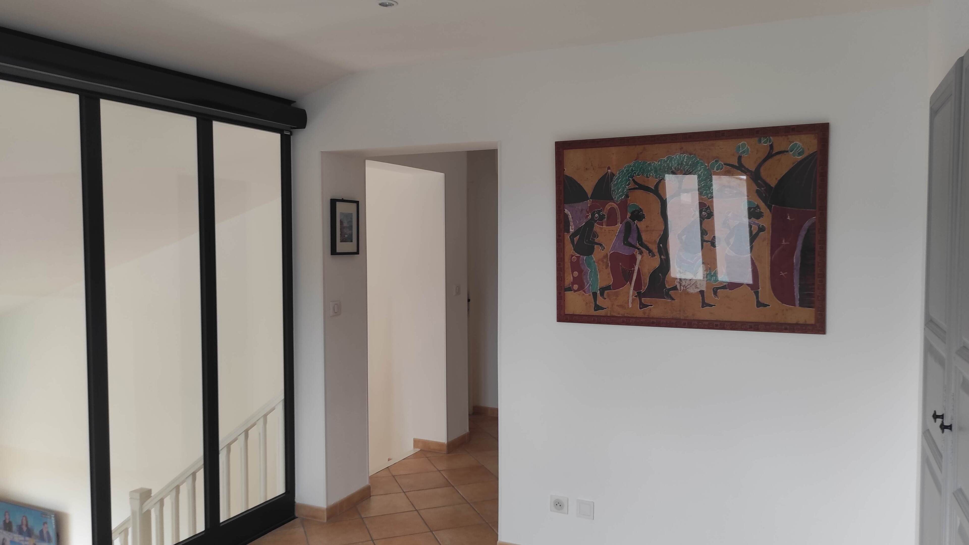 Un pasillo con un cuadro grande en la pared, una puerta corredera y suelo de baldosas.