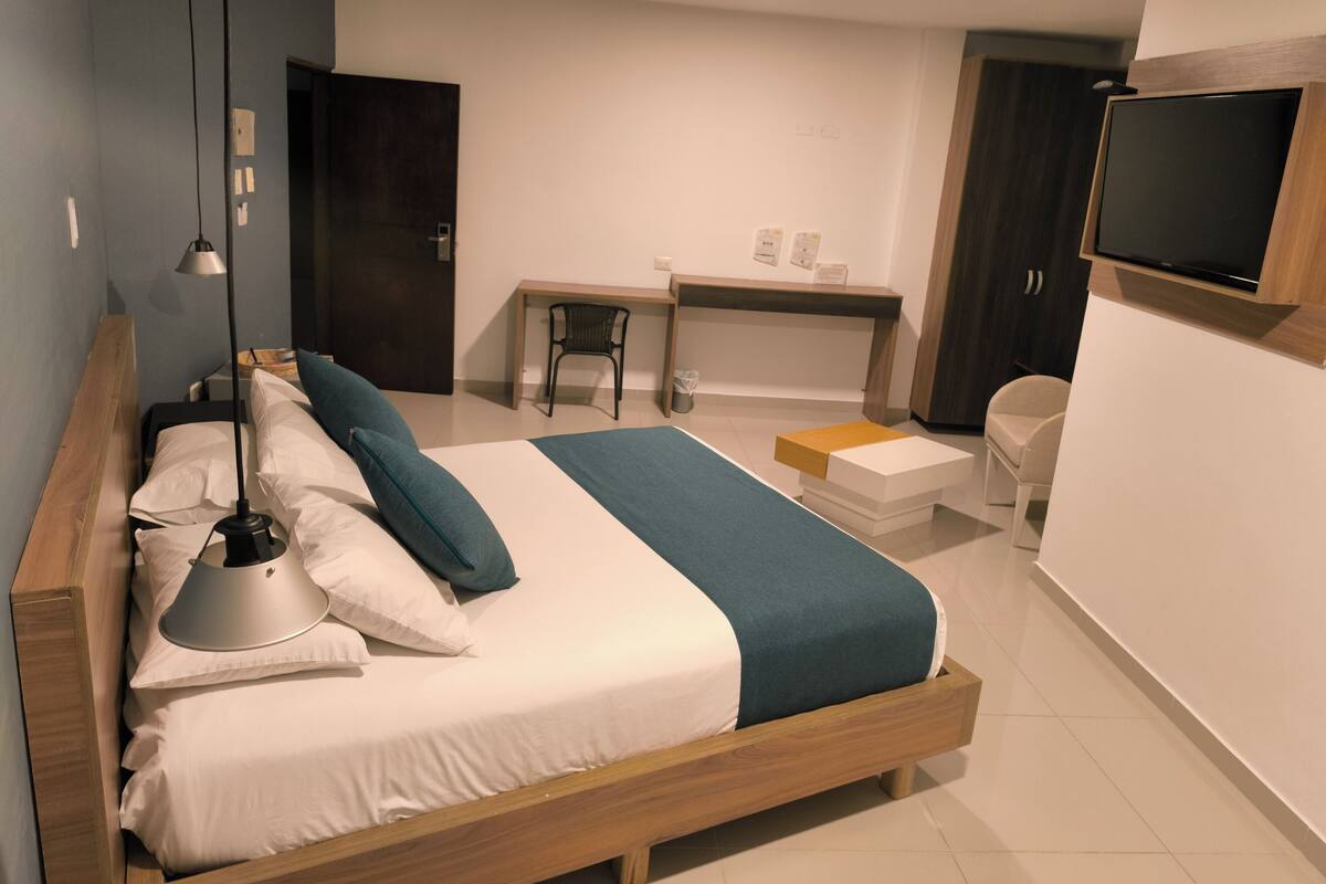 A modern bedroom with a wooden bed, a desk, a chair, and a TV mounted on the wall.