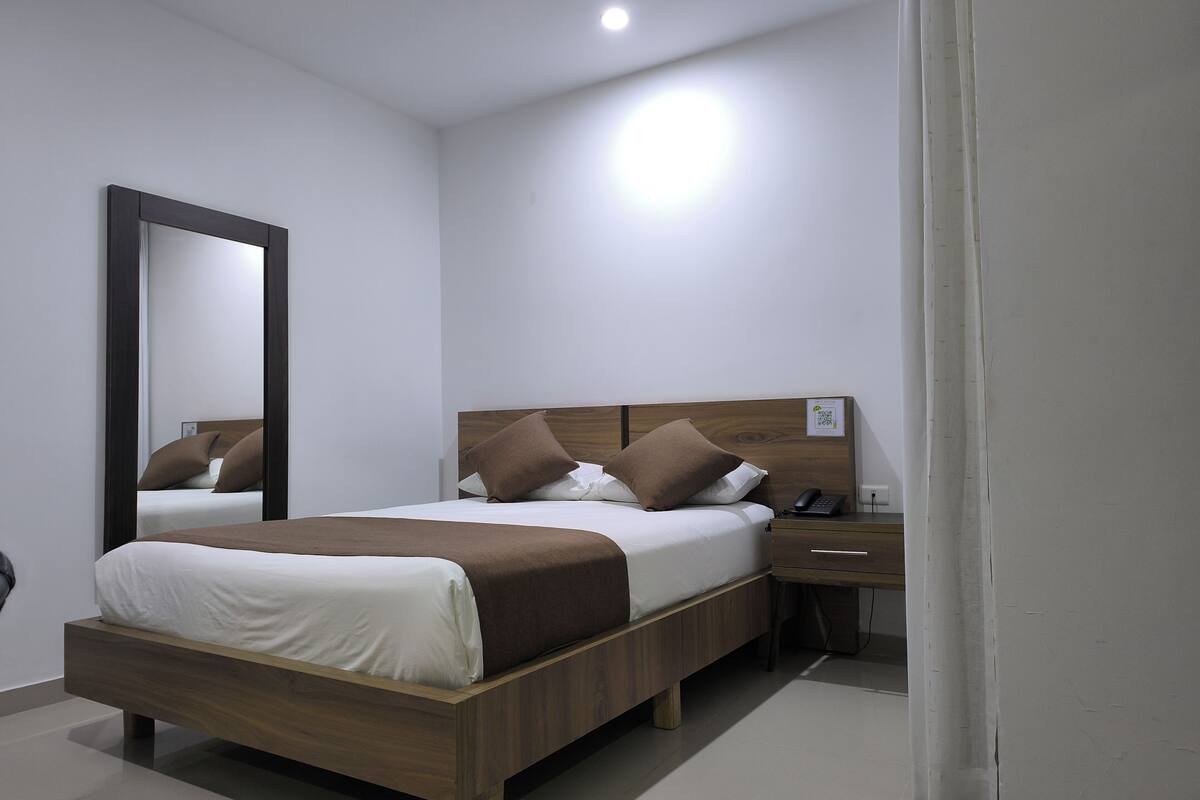 A modern hotel room with a wooden bed, white bedding, a nightstand, a mirror, and a bedside table.