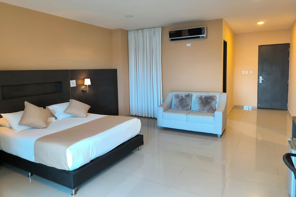 A hotel room with a large bed, a sofa, a wall-mounted air conditioner, and a door.