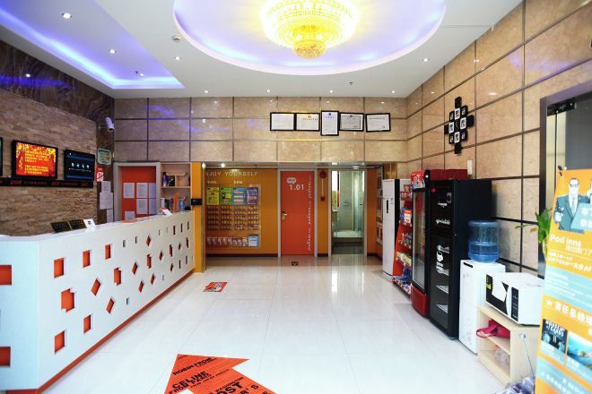 A hotel reception area with a modern design, including a reception desk, a chandelier, and a wall with framed certificates.