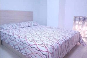 A bed with a patterned bedspread in a room with a wooden headboard and a window with curtains. - Dingding Hotel (Shanghai New International Expo Center Huaxia East Road Subway Station) (Shanghai)