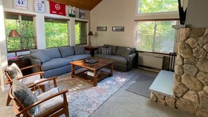 Un salon spacieux avec un haut plafond, de grandes fenêtres, une cheminée en pierre et un coin salon confortable avec un canapé et des fauteuils.