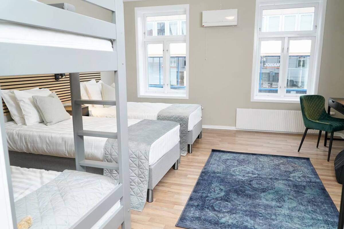 Une chambre avec des lits superposés, un bureau et deux fenêtres.