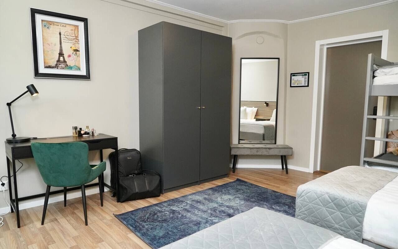 A bedroom with a bed, a desk with a chair, a wardrobe, and a mirror.