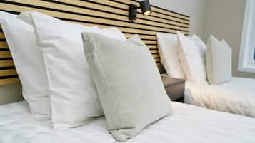 A neatly made bed with white bedding and a variety of pillows, including a textured grey one.