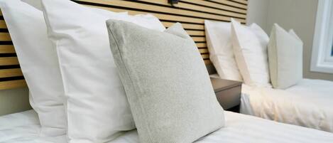 A neatly made bed with white bedding and a variety of pillows, including a textured grey one.