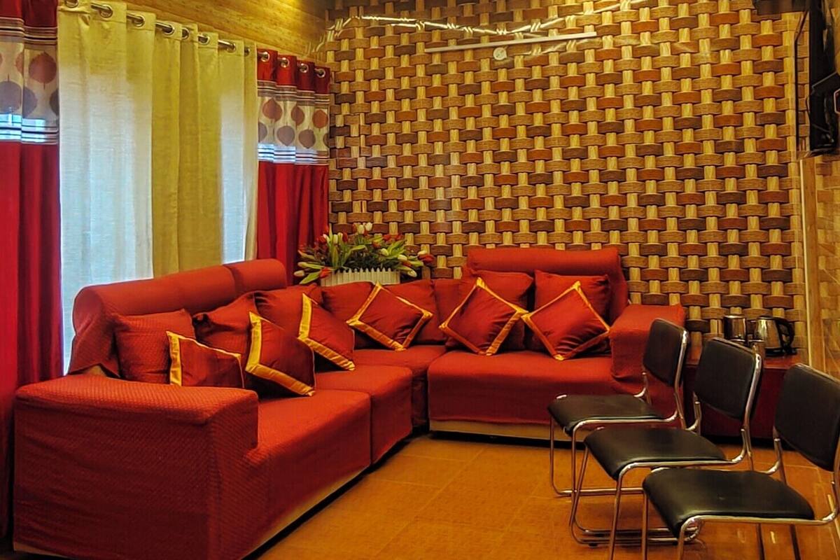Ein modernes Wohnzimmer mit Holzboden, einem roten Ecksofa, schwarzen Sesseln und einer Wand mit Muster.