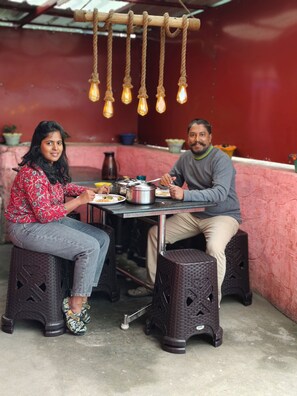 Two people seated at a table with food, under a hanging light fixture. - Mist Cottage & Home Stay (Kodaikanal)
