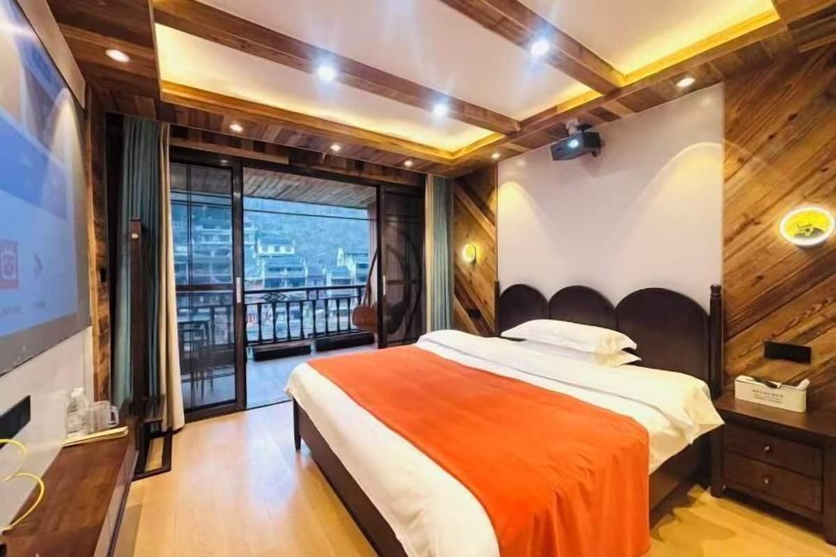 A bedroom with a bed, a nightstand, a TV, and a balcony with a view.