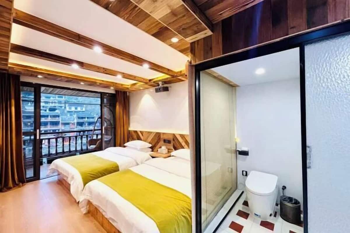 A hotel room with two beds, a balcony, a sliding glass door to a bathroom, and a view of buildings outside.