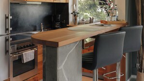 A modern kitchen with wooden cabinets, a central island with bar stools, a built-in oven, and a large window providing natural light.