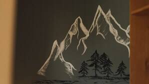 A bedroom with a bed, pillows, and a wall mural of mountains.