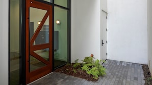 Una entrada moderna con puerta de madera, paneles de vidrio y un pequeño jardín con helechos.