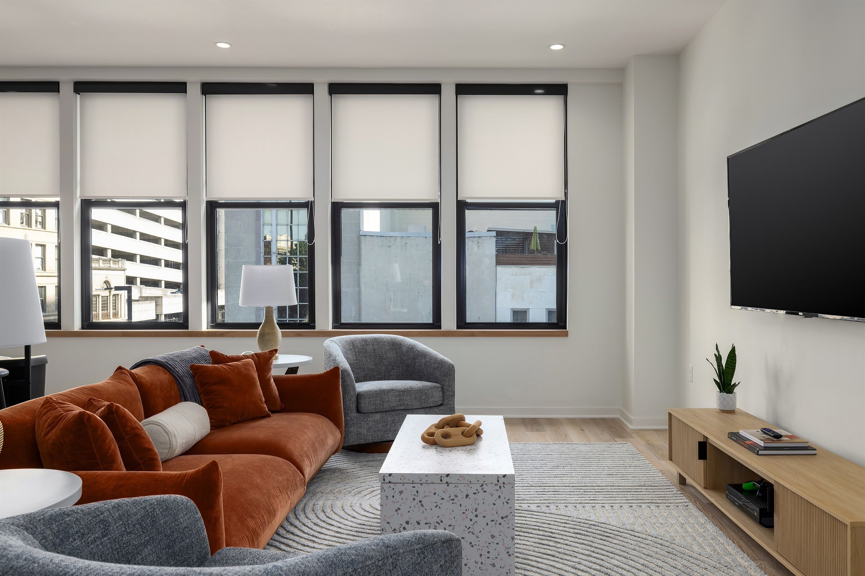 A modern living room with a sofa, armchair, coffee table, and a TV mounted on the wall.