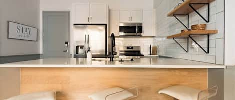 A modern kitchen with white cabinets, stainless steel appliances, and a wooden island with bar stools.