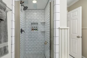 A bathroom with white subway tiles, a shower with a glass door, and a small shelf with toiletries. - Forest Park Gem: Near attractions & Group Fun (Birmingham)
