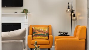 Un salon avec une cheminée, deux fauteuils orange, un lampadaire noir et une petite table sur laquelle est posé un objet décoratif.