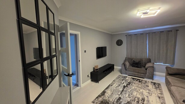 A living room with a sofa, a TV, a rug, and a door leading to another room.