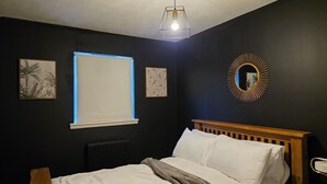 A bedroom with a bed, a window with blinds, a radiator, and a wall-mounted mirror.